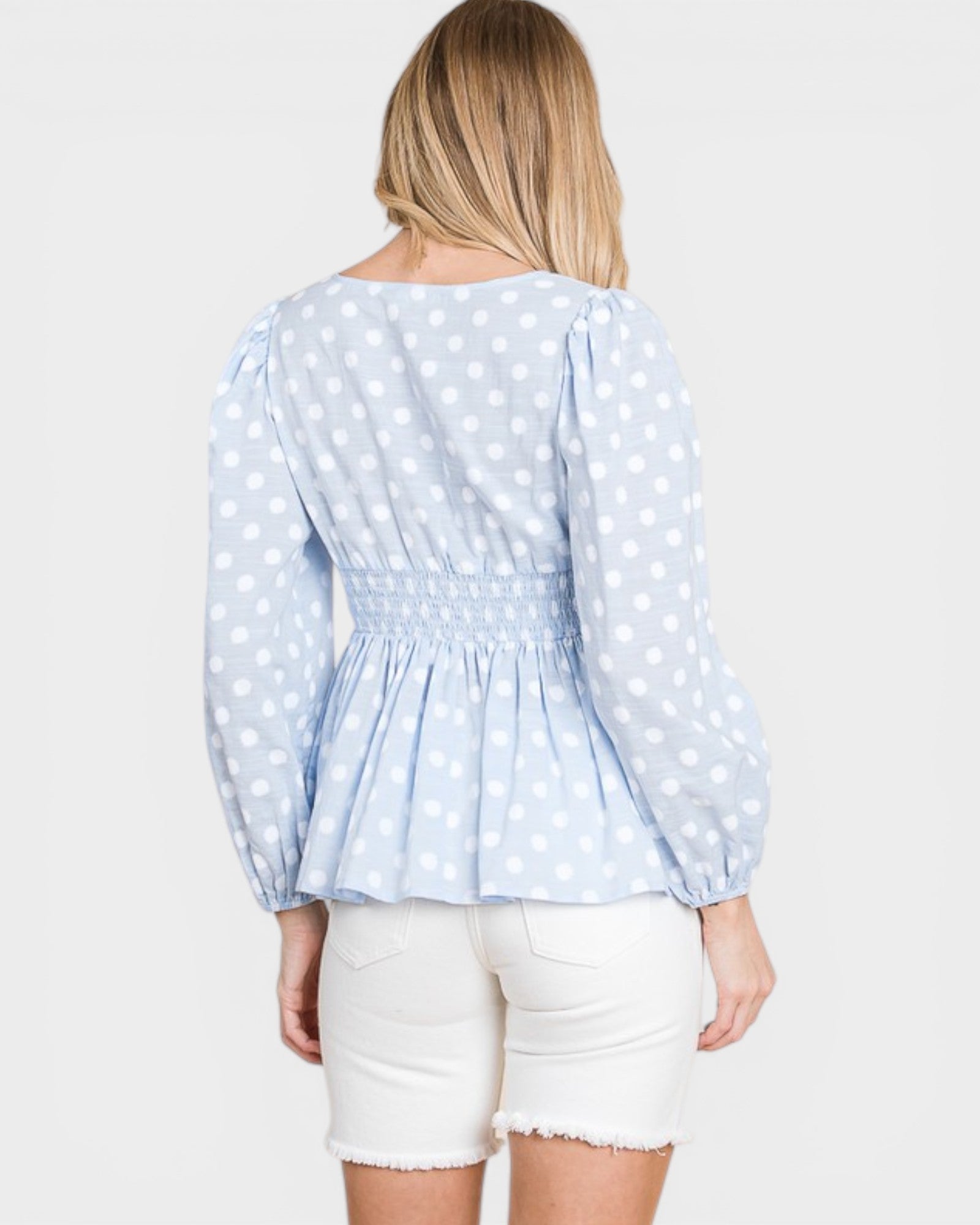 Woman wearing a light blue polka dot blouse and white shorts on a white background
