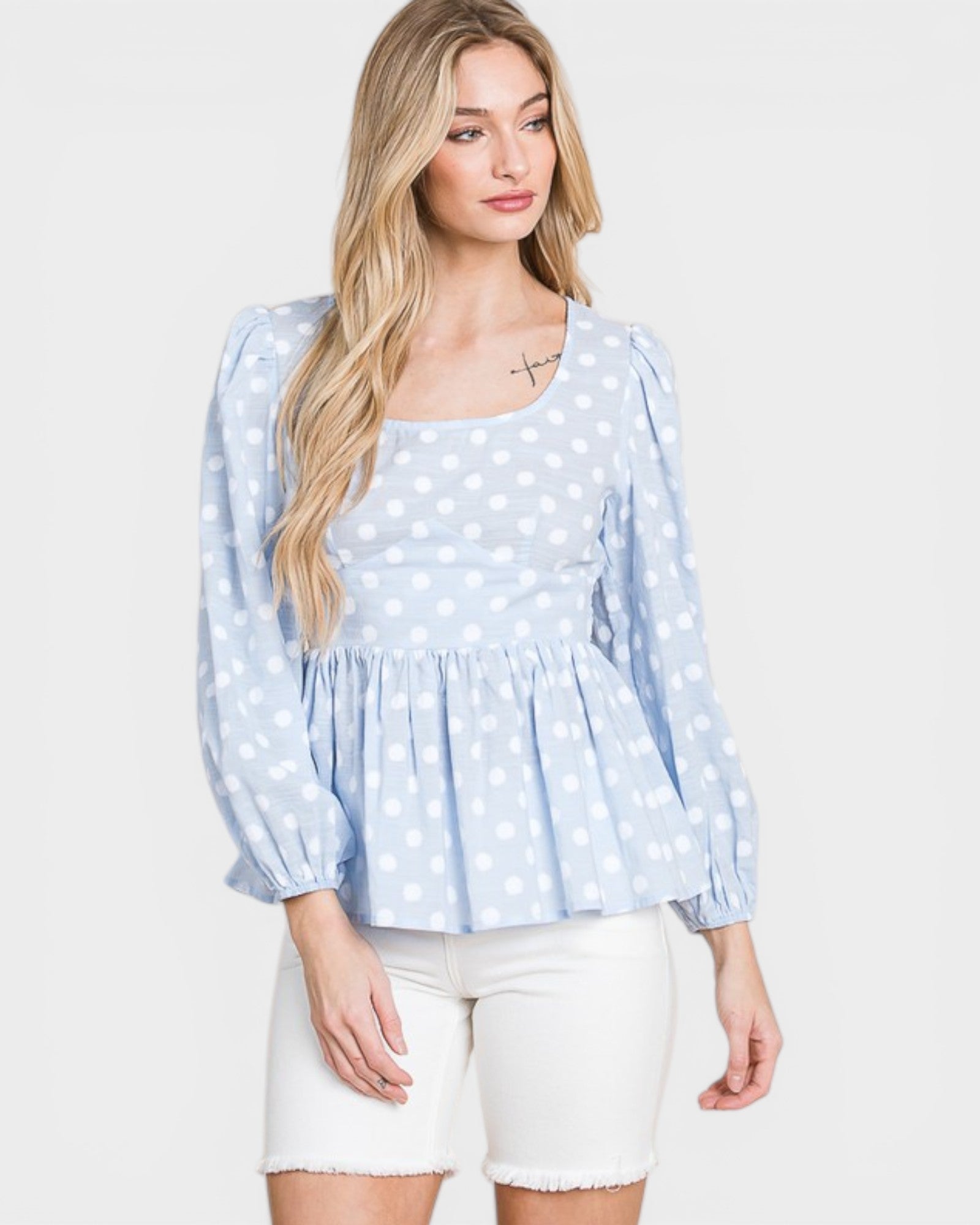 Woman wearing a light blue polka dot blouse with white shorts on a plain background