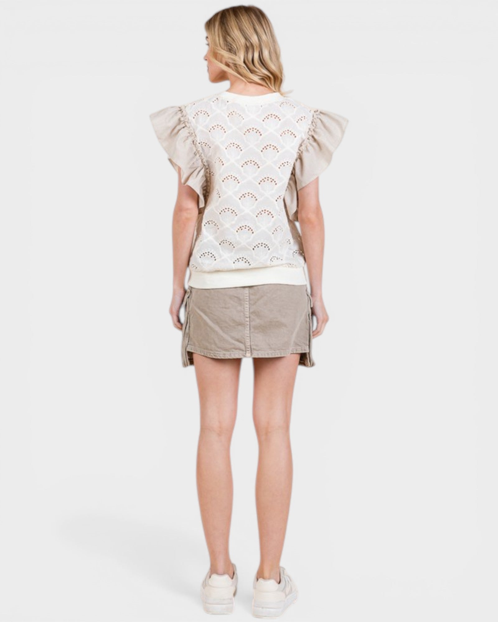 Woman wearing a light-colored top with ruffled sleeves and a matching skirt on a white background