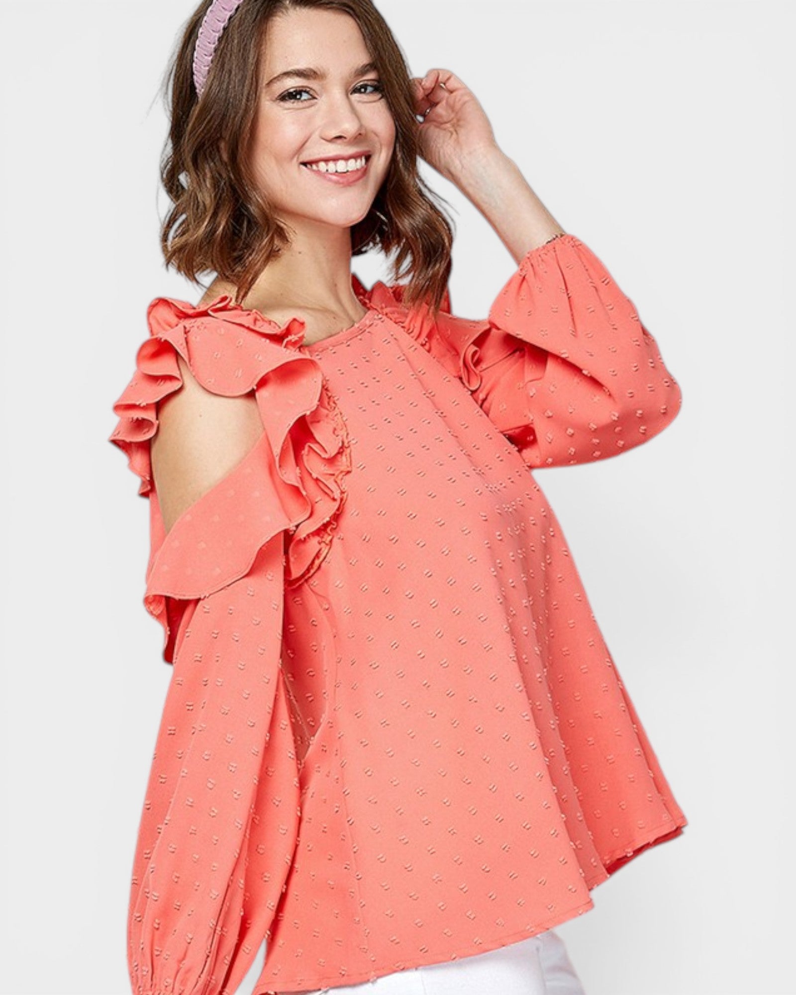 Woman wearing a coral blouse with ruffled sleeves on a white background