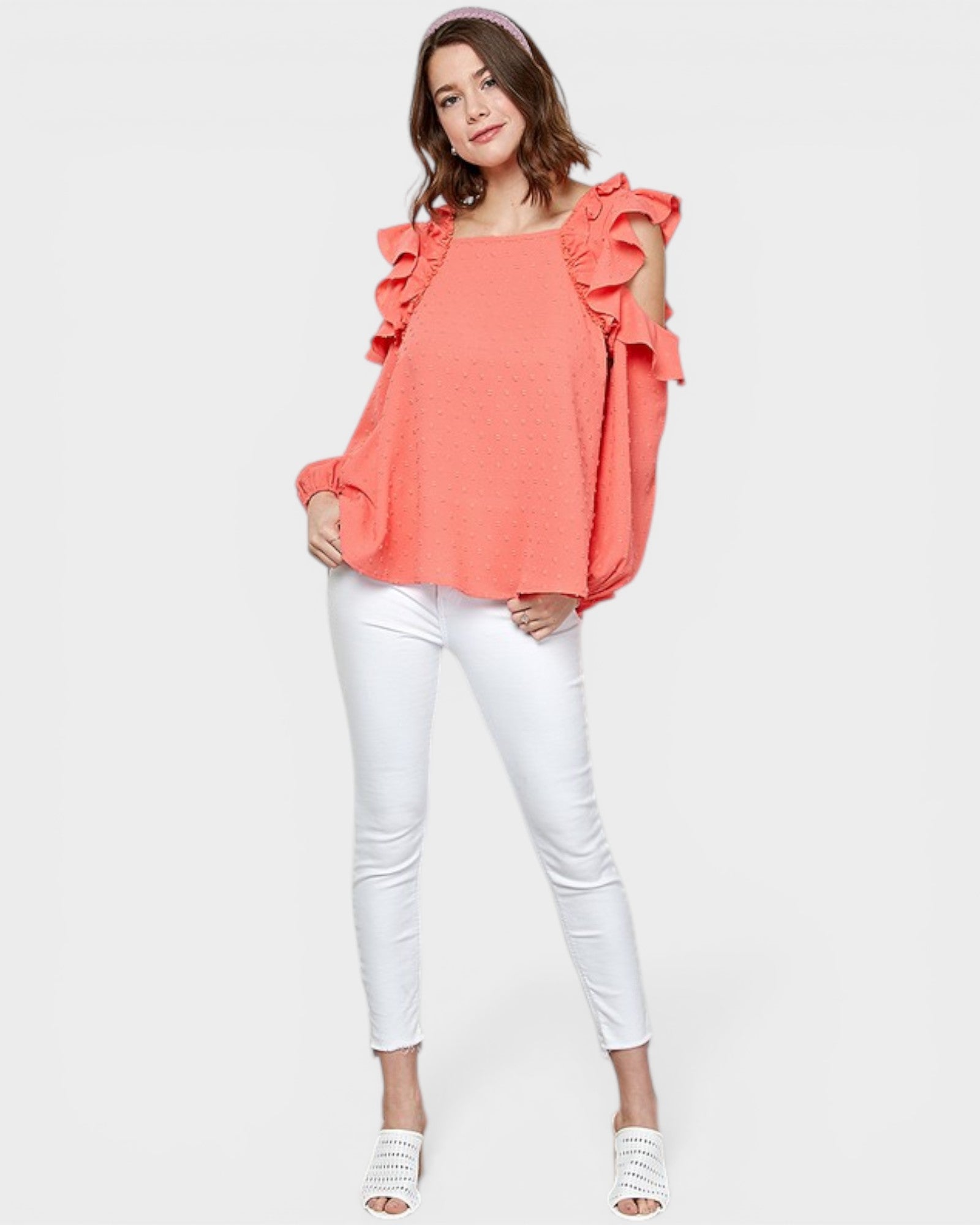 Woman wearing a coral top with ruffled shoulders and white pants on a white background