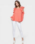 Woman wearing a coral top with ruffled shoulders and white pants on a white background