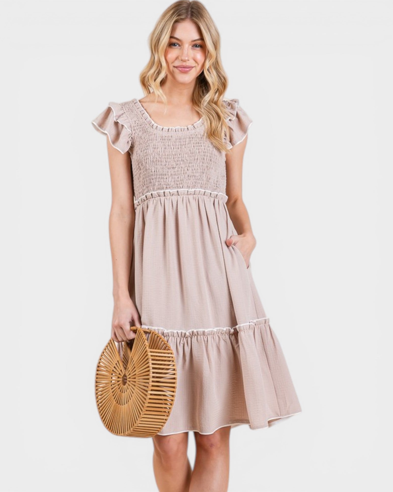 Woman wearing a beige dress holding a woven bag on a white background