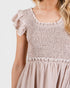 Close-up of a person wearing a light brown smocked dress with ruffled sleeves on a white background.
