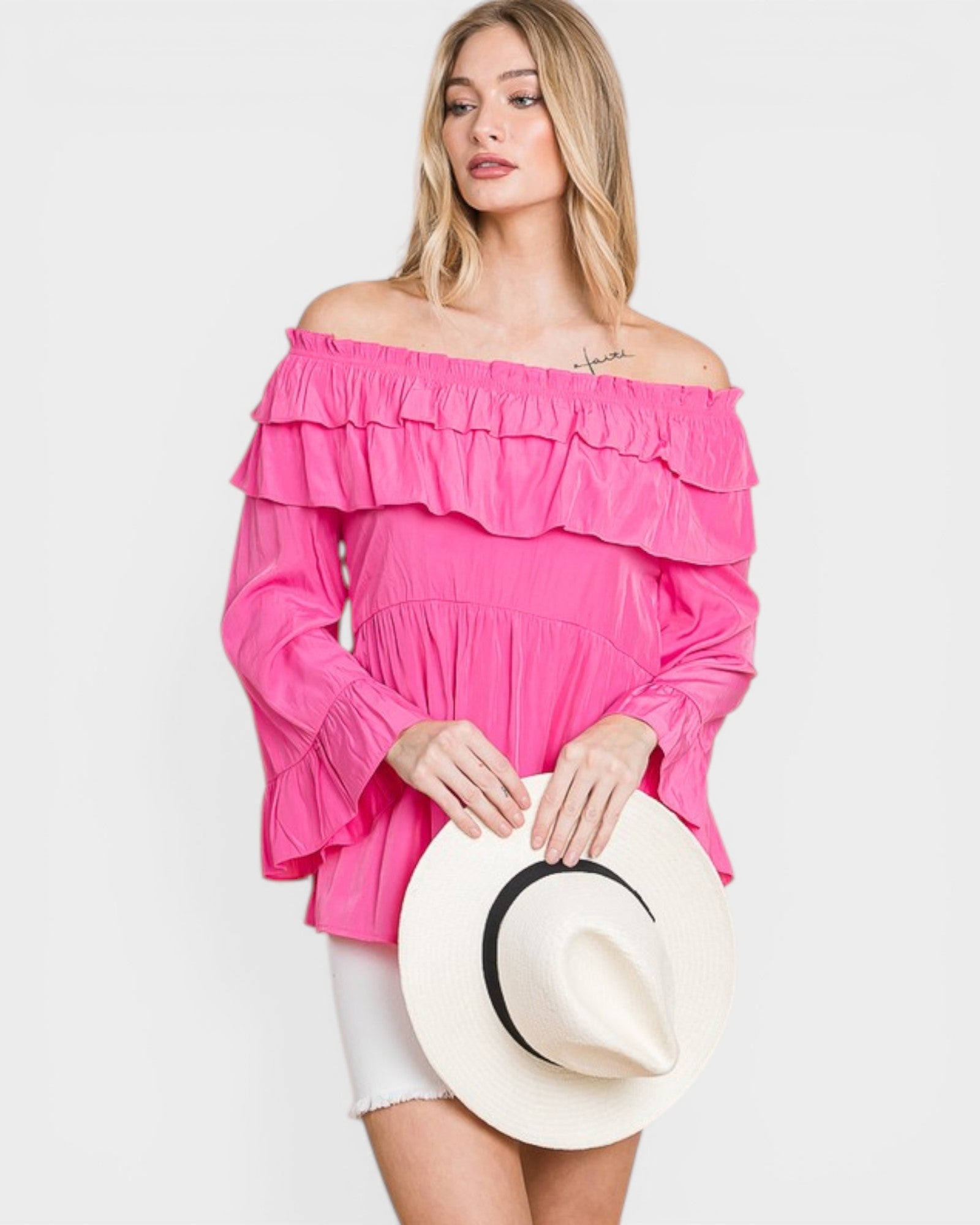 Woman wearing a pink off-shoulder top holding a white hat on a light gray background