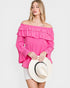 Woman wearing a pink off-shoulder top holding a white hat on a light gray background