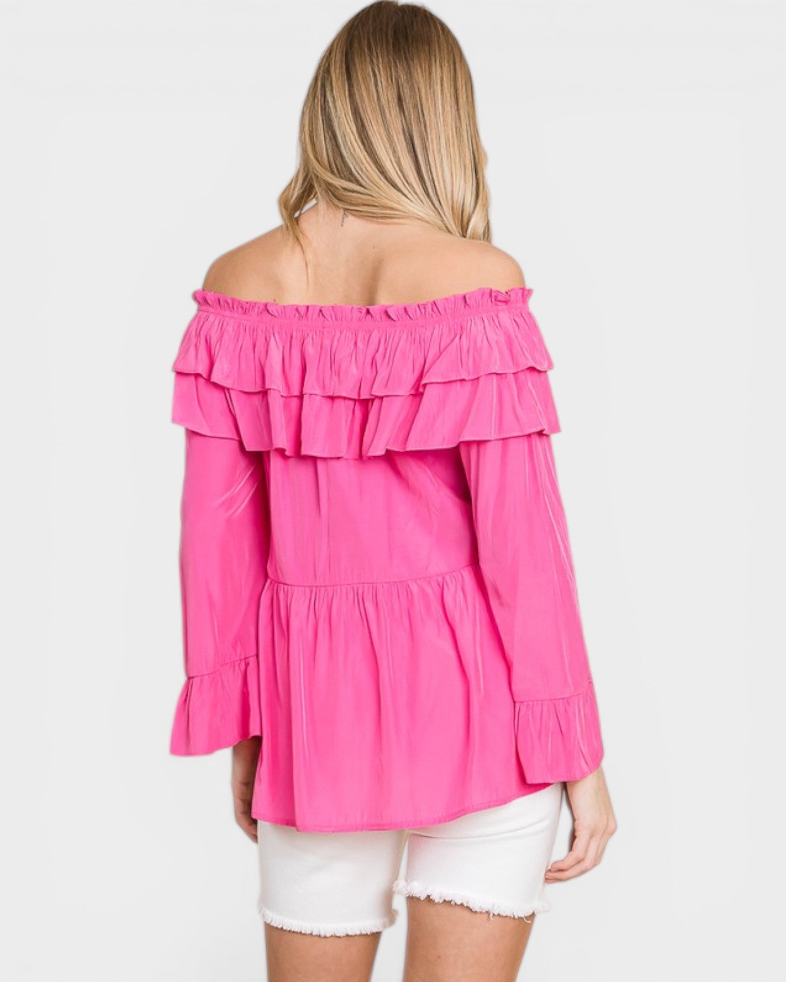 Woman wearing a bright pink off-shoulder top with ruffled layers on a white background