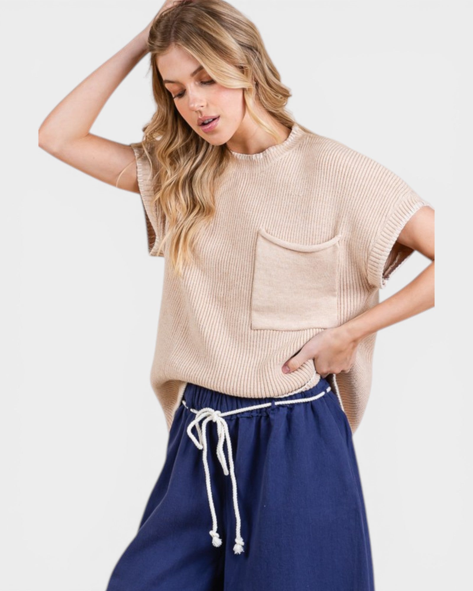 Woman wearing a beige sleeveless sweater with a pocket and blue pants on a white background