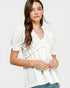 Woman wearing a white blouse with ruffled details on a plain background