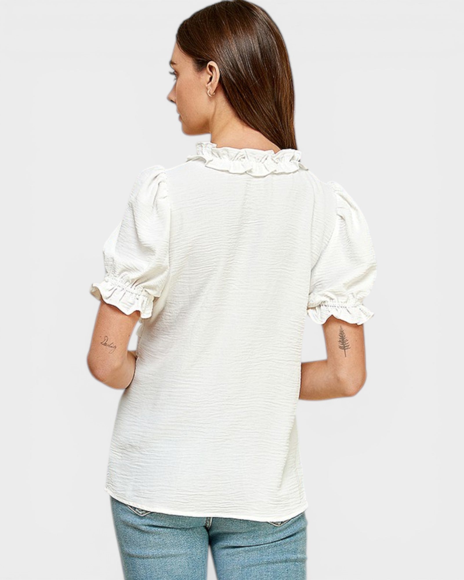 Woman wearing a white blouse with ruffled sleeves on a plain background