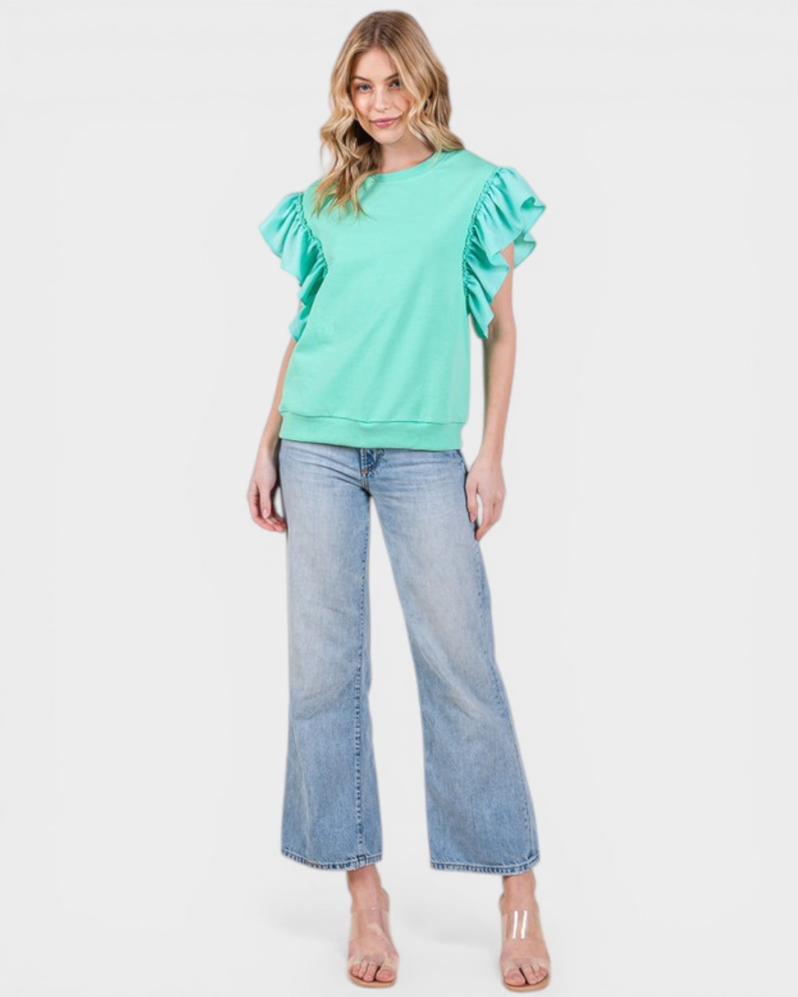 Woman wearing a light green blouse with ruffled sleeves and blue jeans on a white background