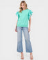 Woman wearing a light green blouse with ruffled sleeves and blue jeans on a white background