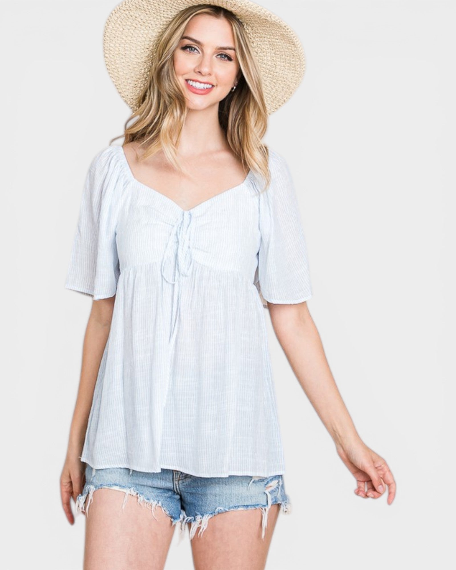 Woman wearing a light blue top and denim shorts with a straw hat on a white background