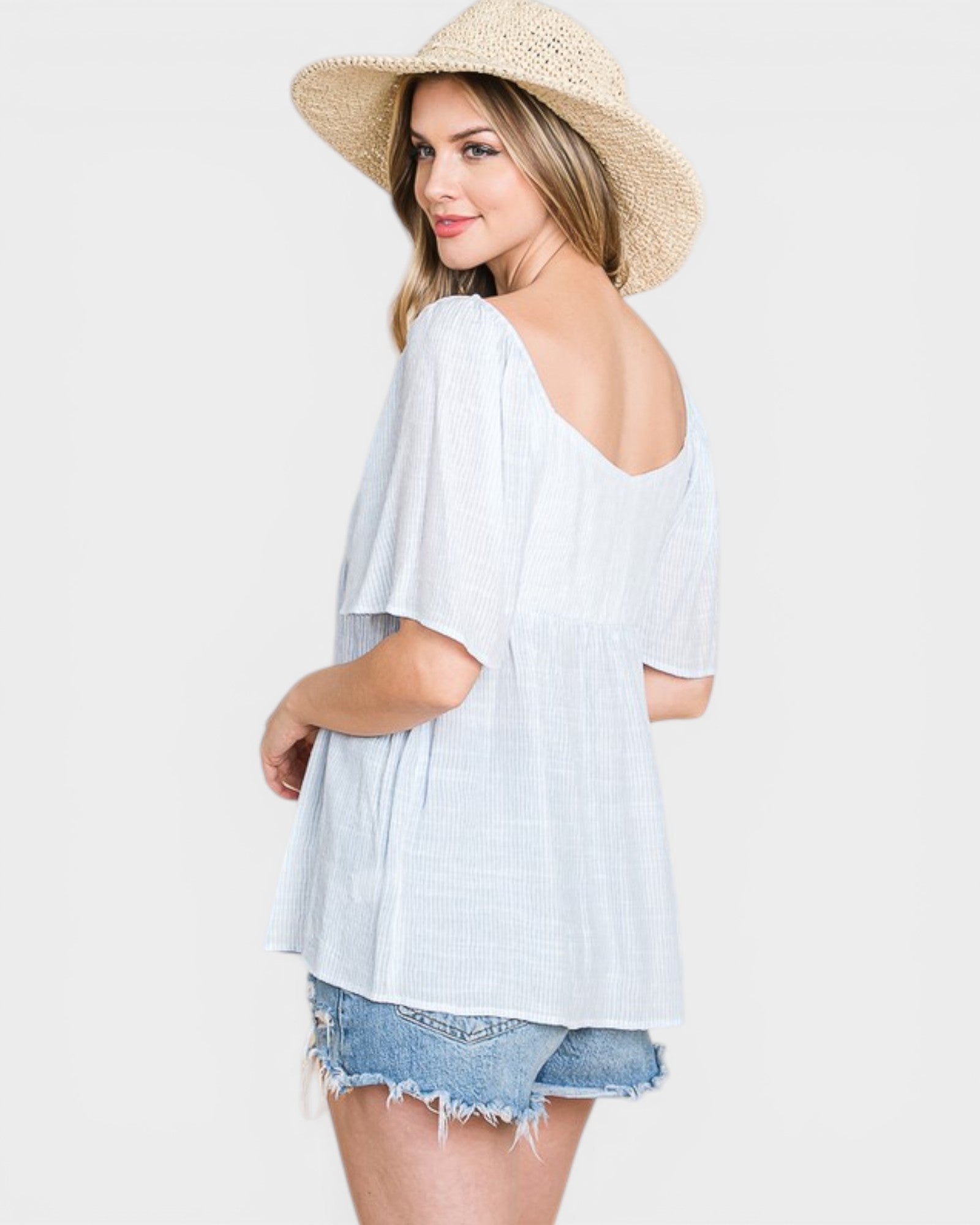 Woman wearing a light blue off-shoulder top and denim shorts with a straw hat on a white background