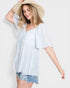 Woman wearing a light blue blouse and denim shorts with a straw hat on a white background