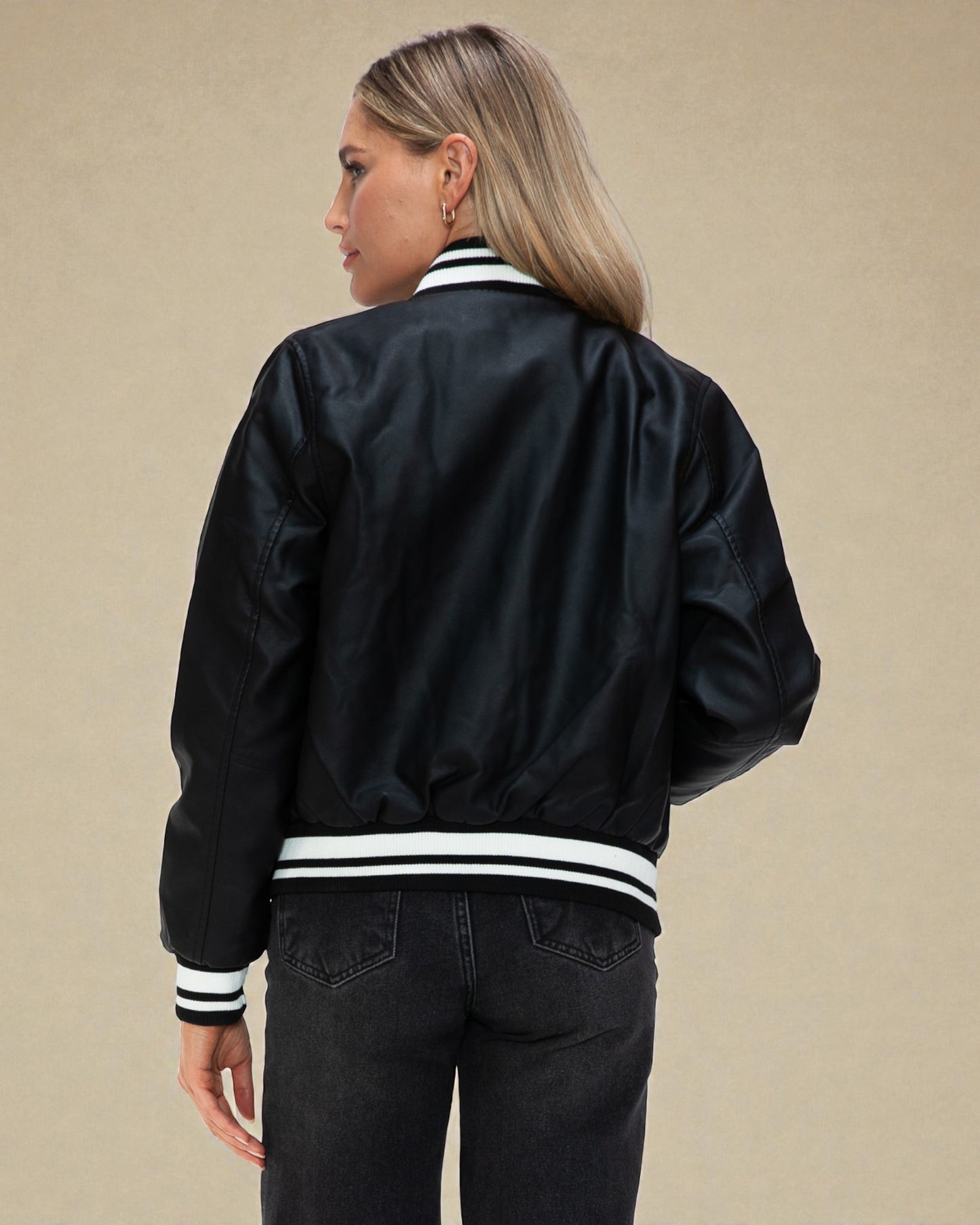 Person wearing a black bomber jacket with white stripes on a beige background