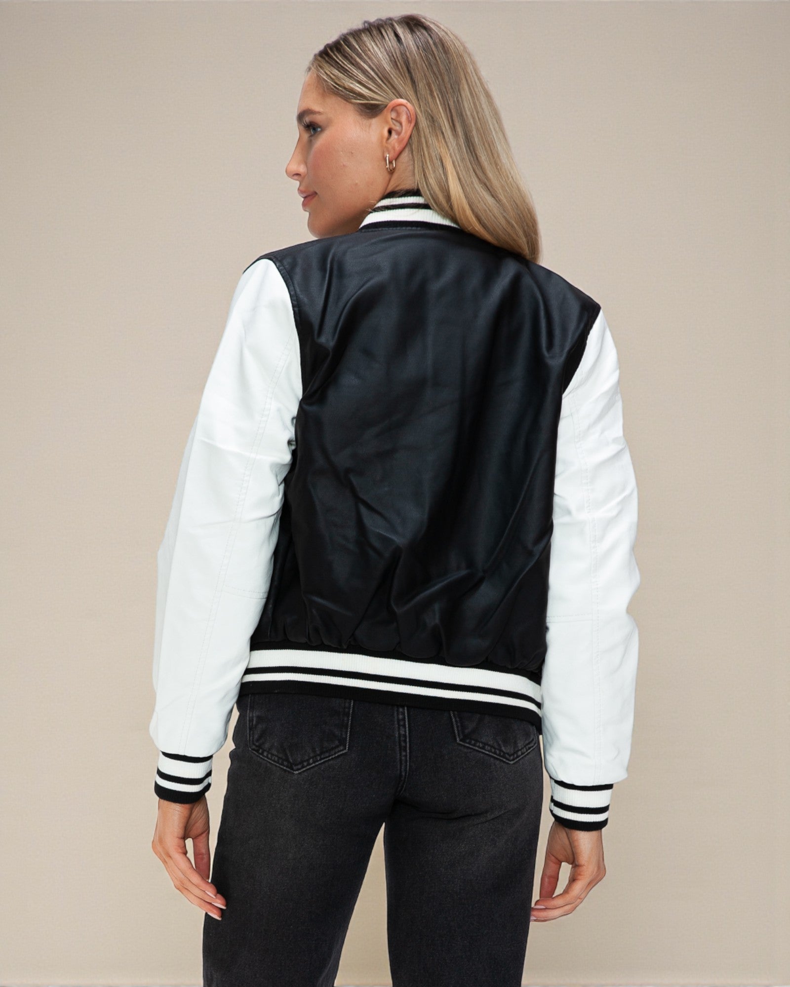 Person wearing a black and white varsity jacket on a beige background