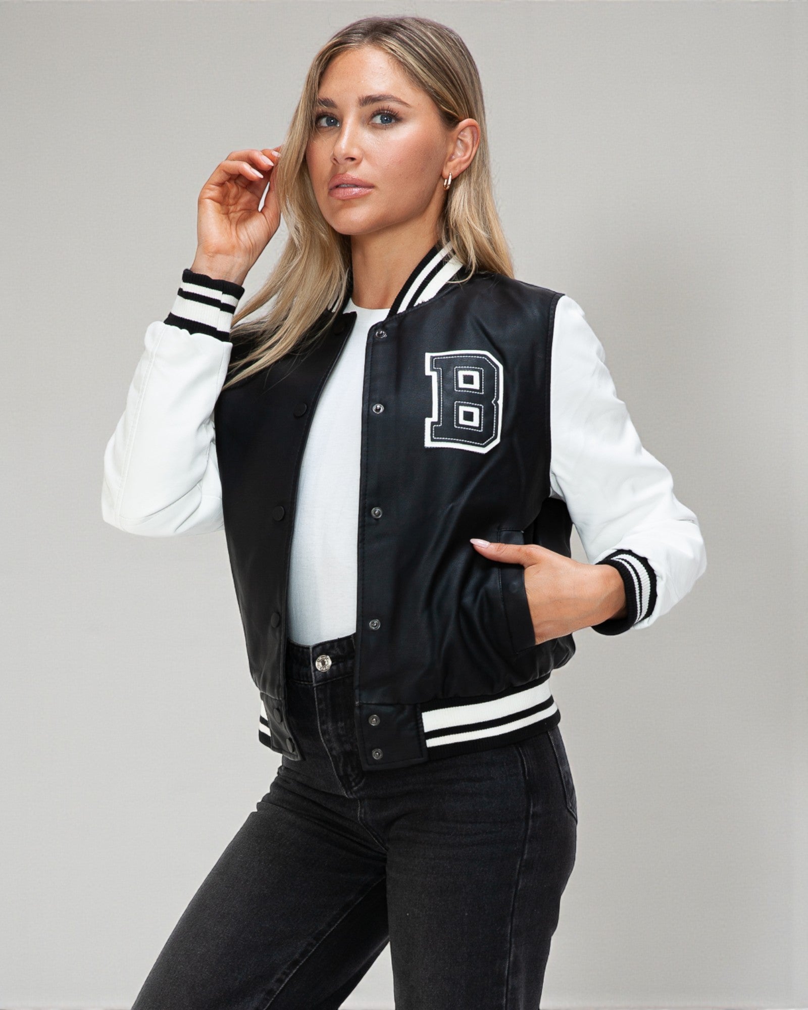 Woman wearing a black and white varsity jacket with a letter 'B' on a gray background