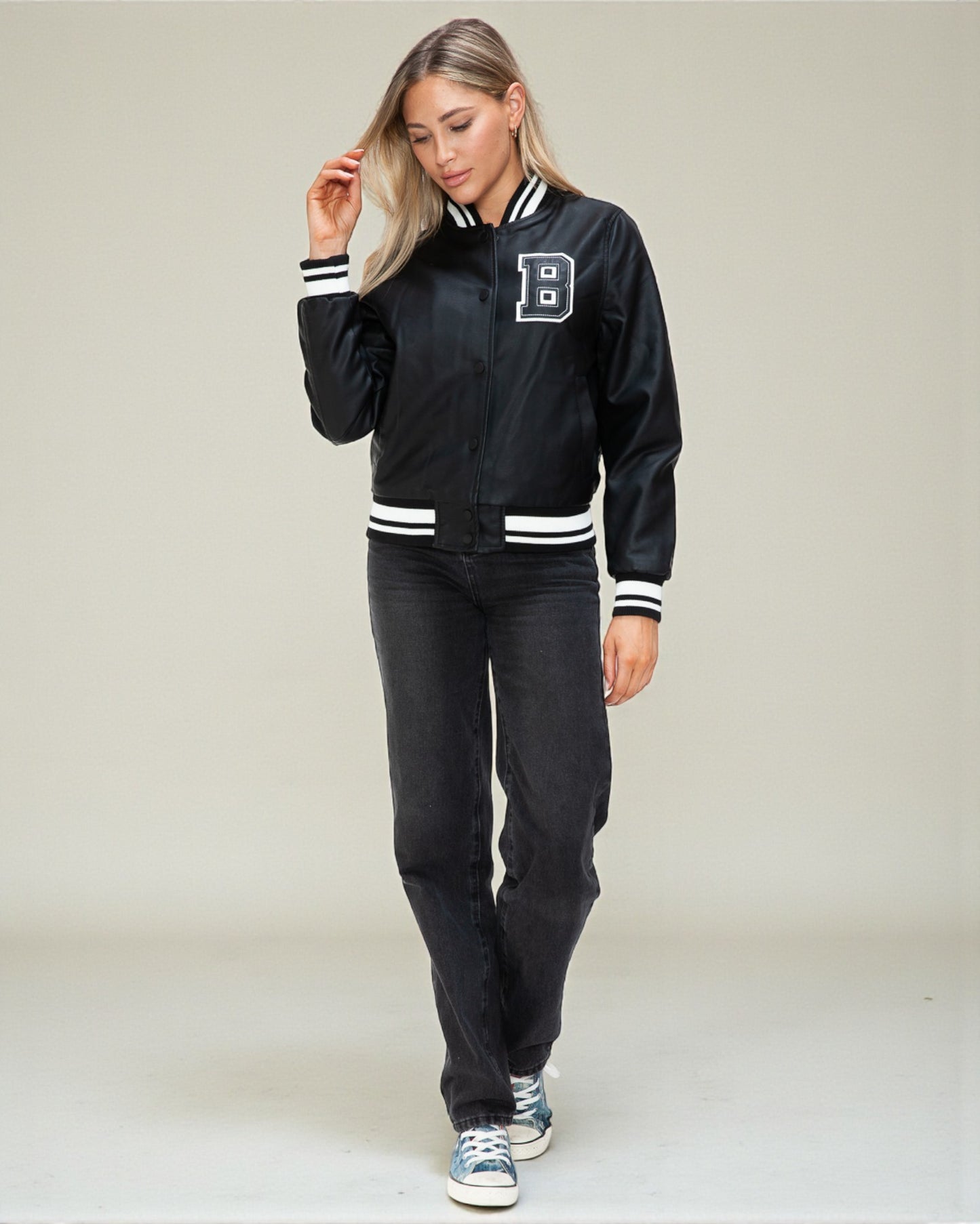 Woman wearing a black varsity jacket with white accents on a plain background