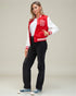 Person wearing a red and white varsity jacket with a logo, white shirt, black pants, and blue sneakers on a plain background.