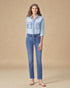 Woman wearing a light blue denim shirt and jeans on a beige background