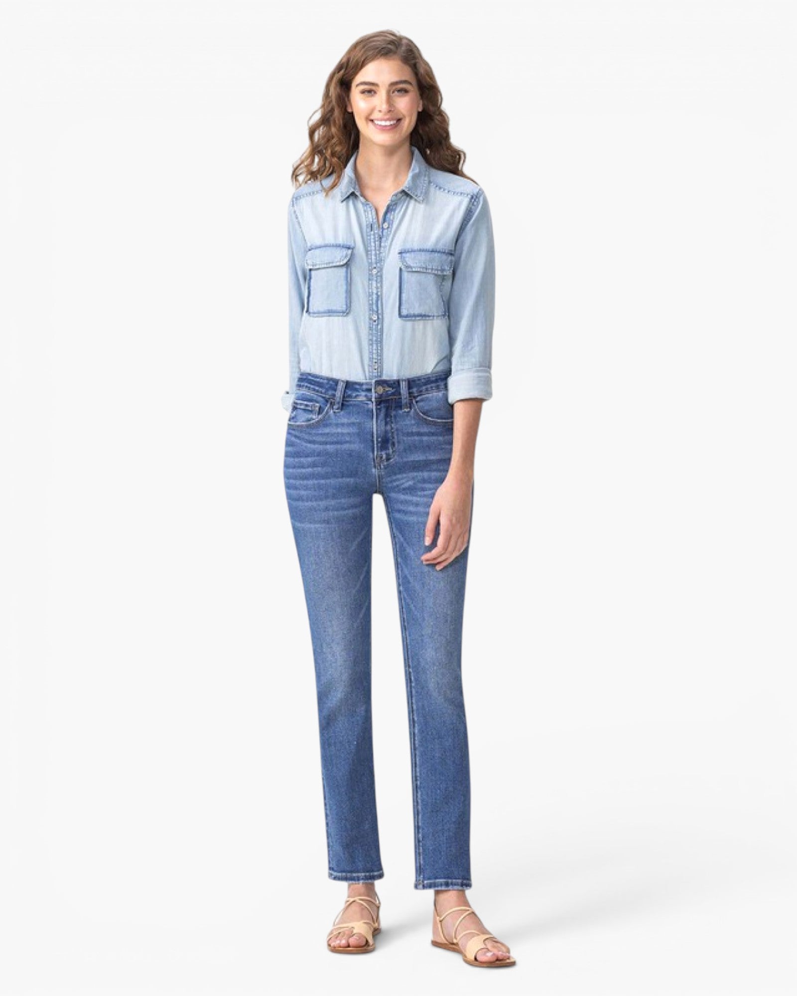 A woman modeling a light blue denim button-up shirt with chest pockets and medium-wash blue straight-leg jeans, standing against a plain white studio background.