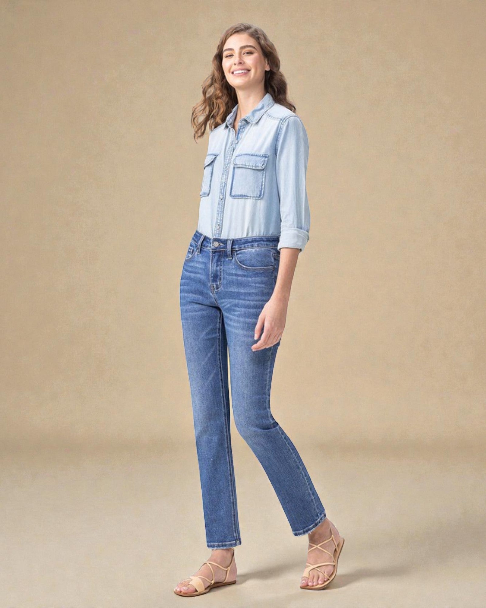 Woman wearing a light blue denim shirt and jeans on a beige background