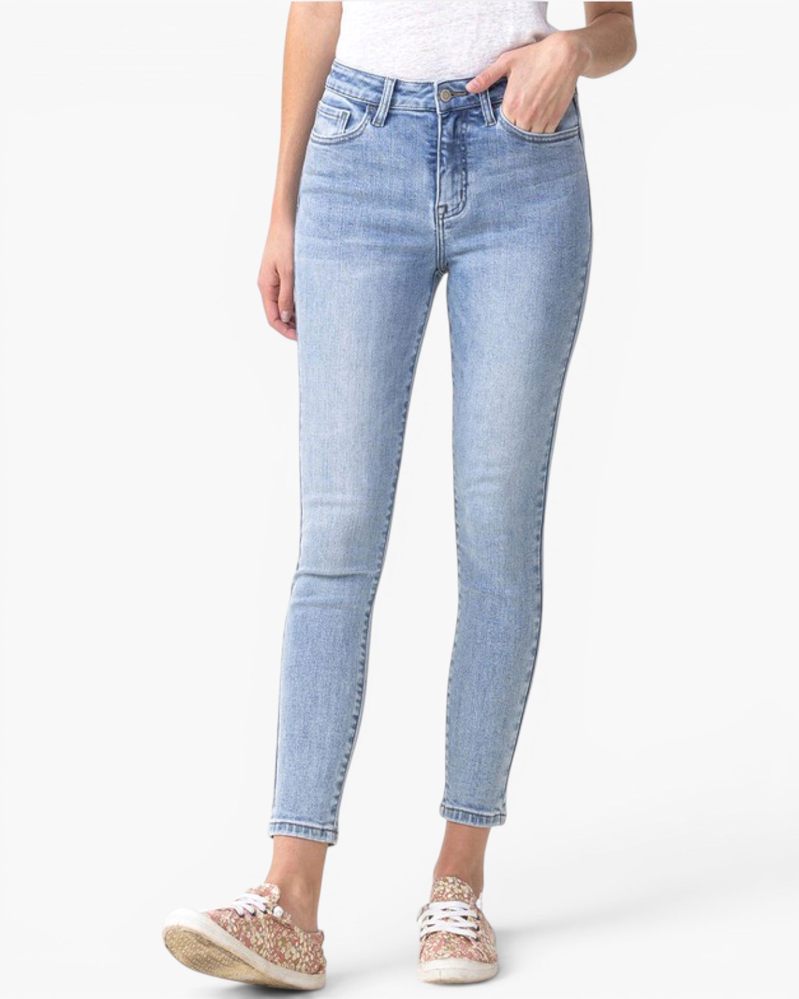 A person wearing light-wash blue skinny jeans with a white top and patterned sneakers, shown from the waist down against a plain white studio background.