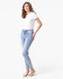 A woman modeling light-wash blue skinny jeans with a white t-shirt and beige lace-up sneakers, standing against a solid white background.