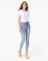 A woman modeling light-wash blue skinny jeans with a white short-sleeve t-shirt and beige lace-up sandals, standing against a plain white studio background.