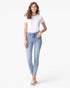 A woman modeling light-wash blue skinny jeans with a white short-sleeve t-shirt and white sneakers, standing against a plain white studio background.