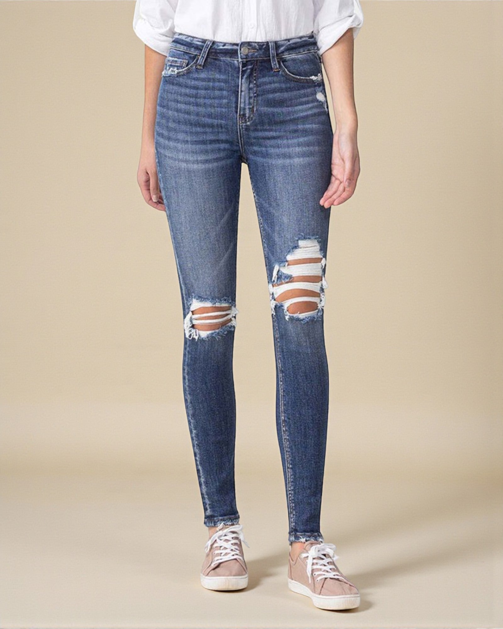 Person wearing distressed blue jeans on a beige background