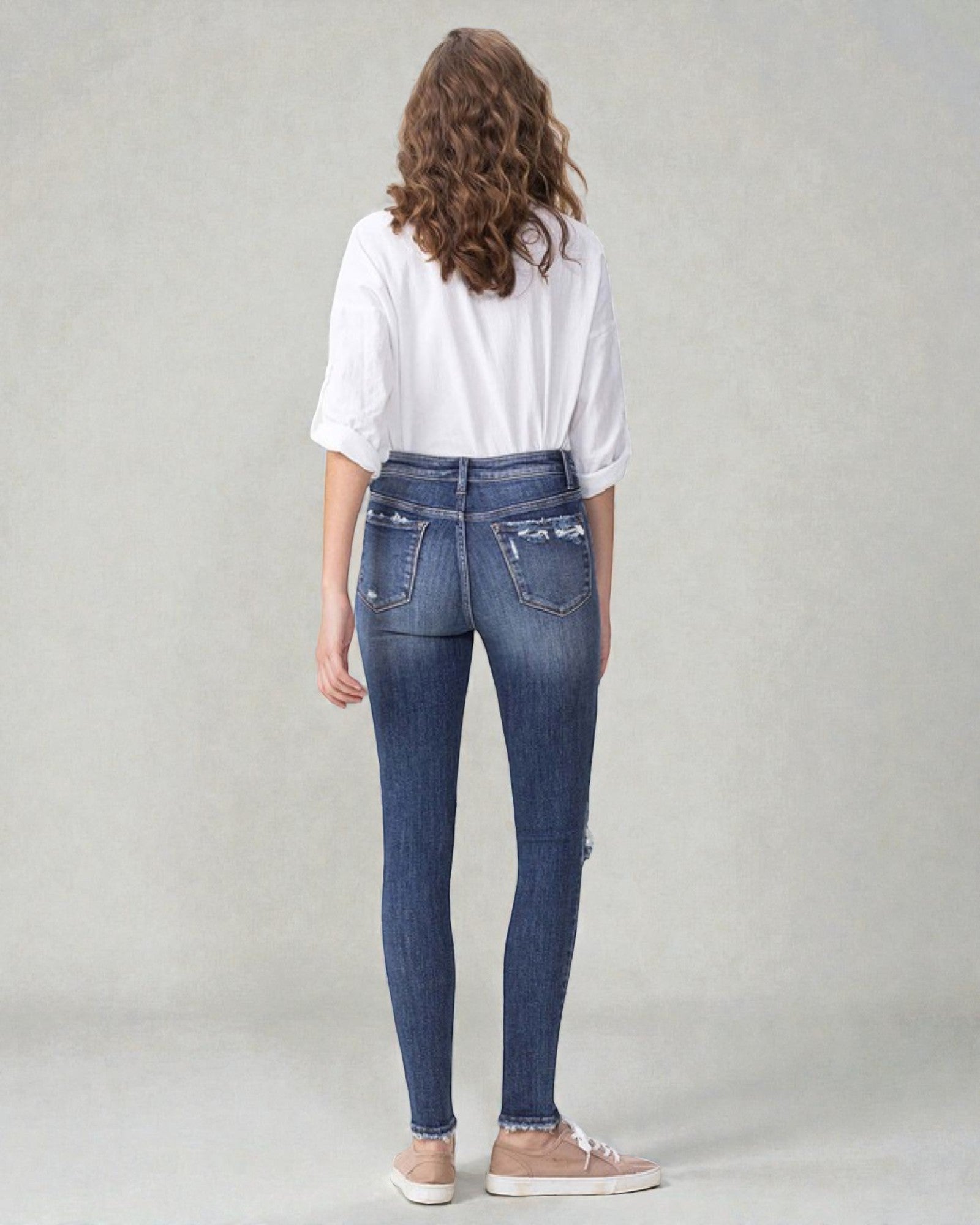 Person wearing blue jeans and a white shirt on a plain background