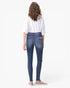 A woman shown from the back wearing blue skinny jeans with a white shirt and beige sneakers, photographed against a plain white studio background.