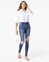 A woman modeling a white button-down shirt and blue distressed skinny jeans with ripped knees, paired with beige sneakers, against a plain white background.