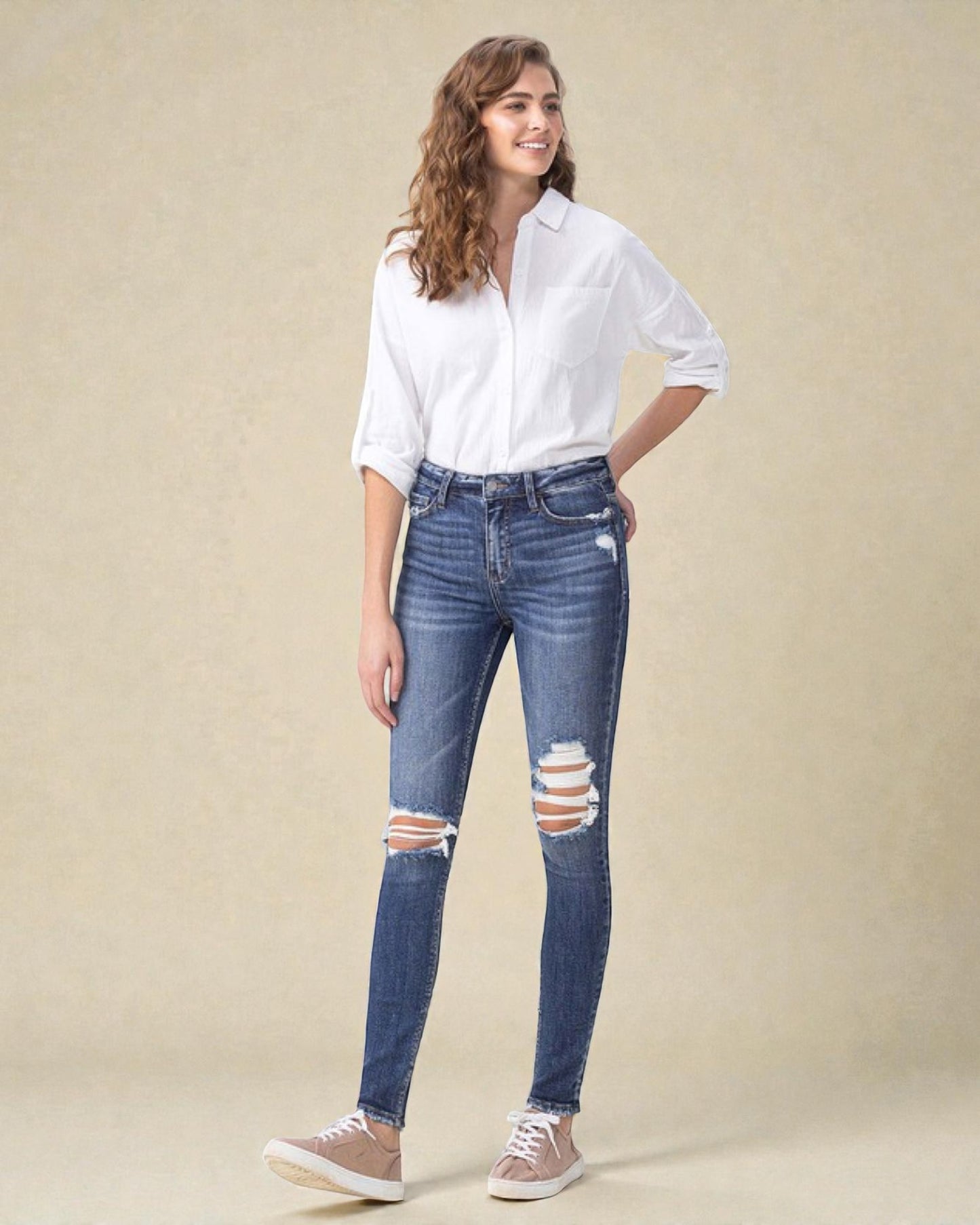 Woman wearing a white shirt and blue jeans with distressed details on a beige background
