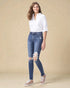 Woman wearing a white shirt and distressed blue jeans against a beige background