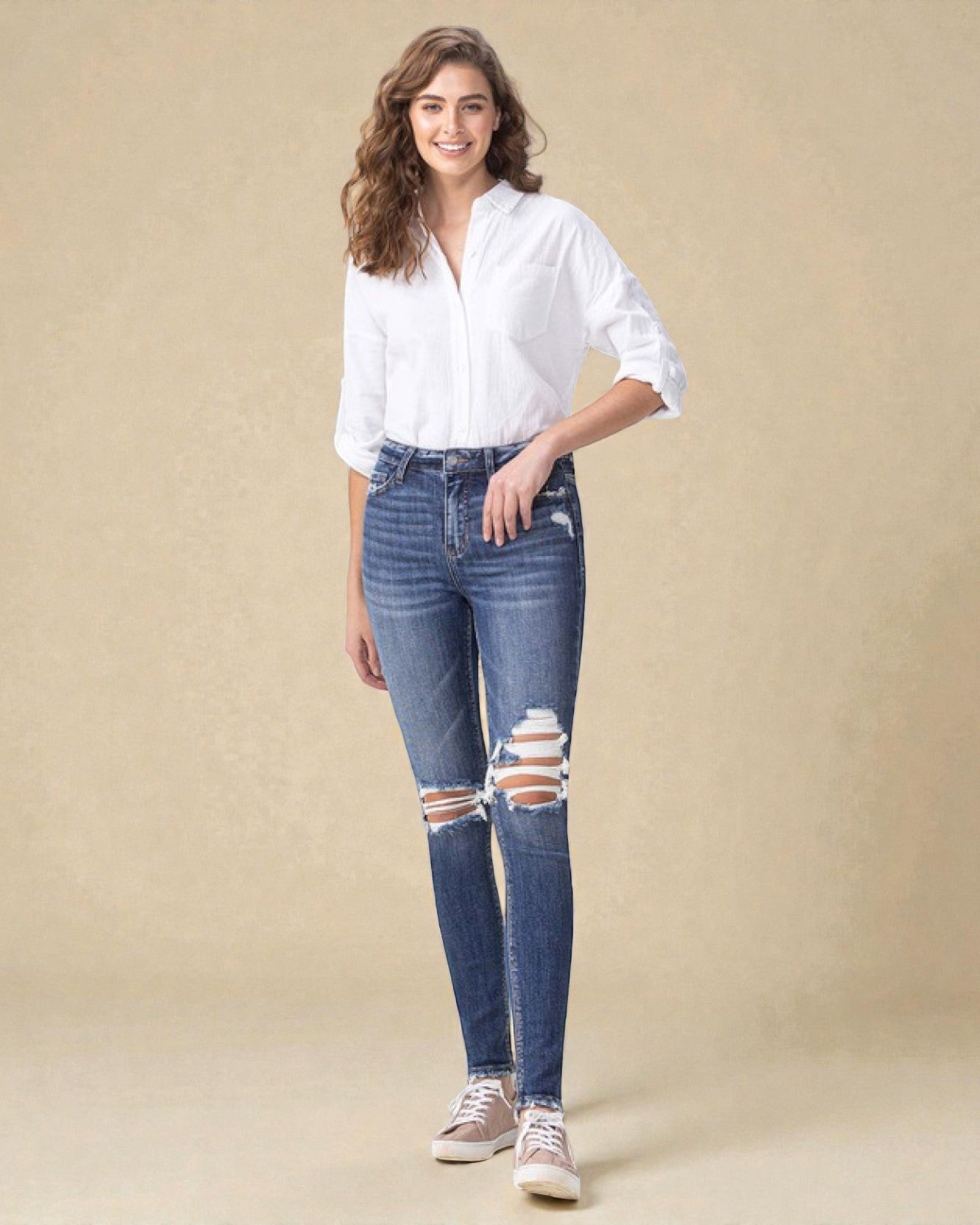 Woman wearing a white shirt and distressed blue jeans on a beige background