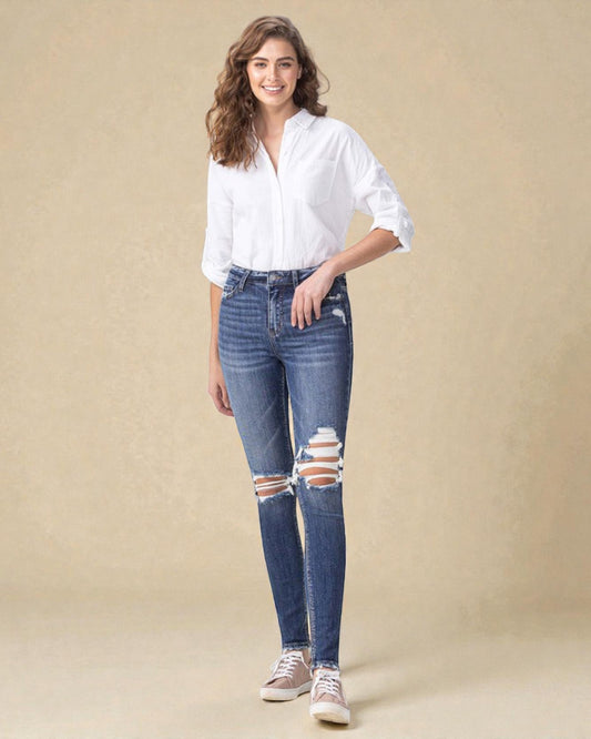 Woman wearing a white shirt and distressed blue jeans on a beige background