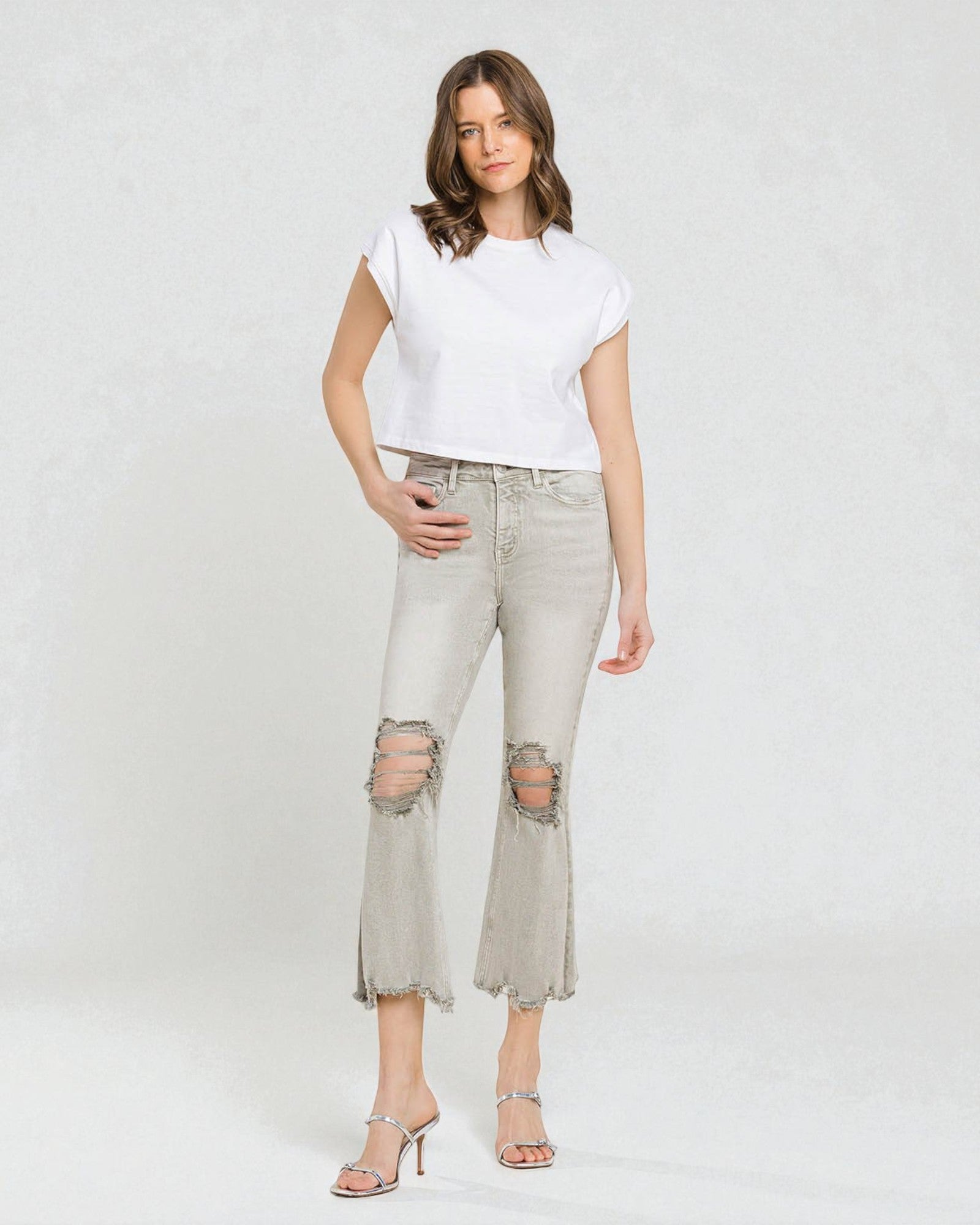 Woman wearing a white t-shirt and light gray ripped jeans on a white background