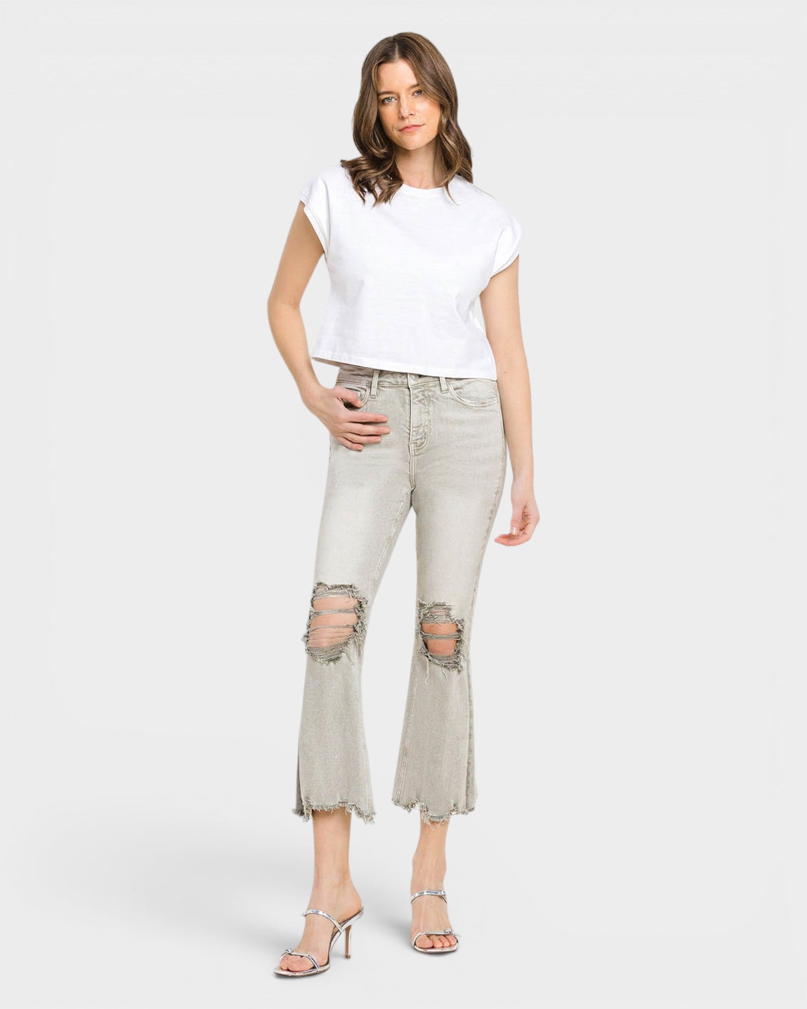 Woman wearing a white top and light gray distressed jeans on a white background