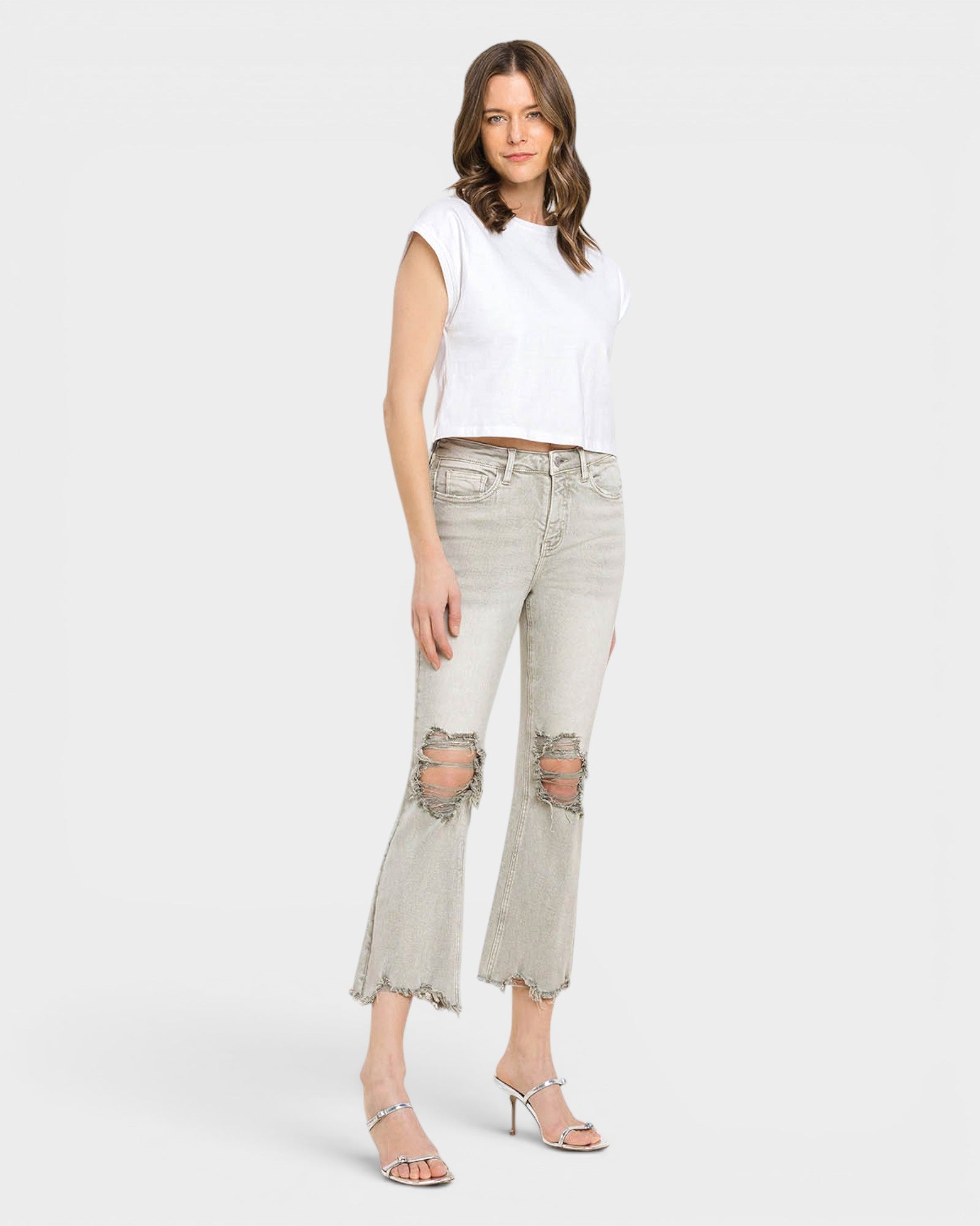 Woman wearing light gray distressed jeans and a white top on a white background