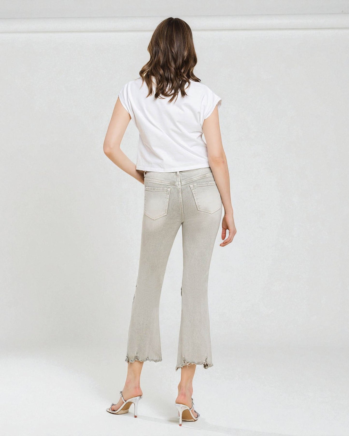 Woman wearing light-colored jeans and a white top on a plain background