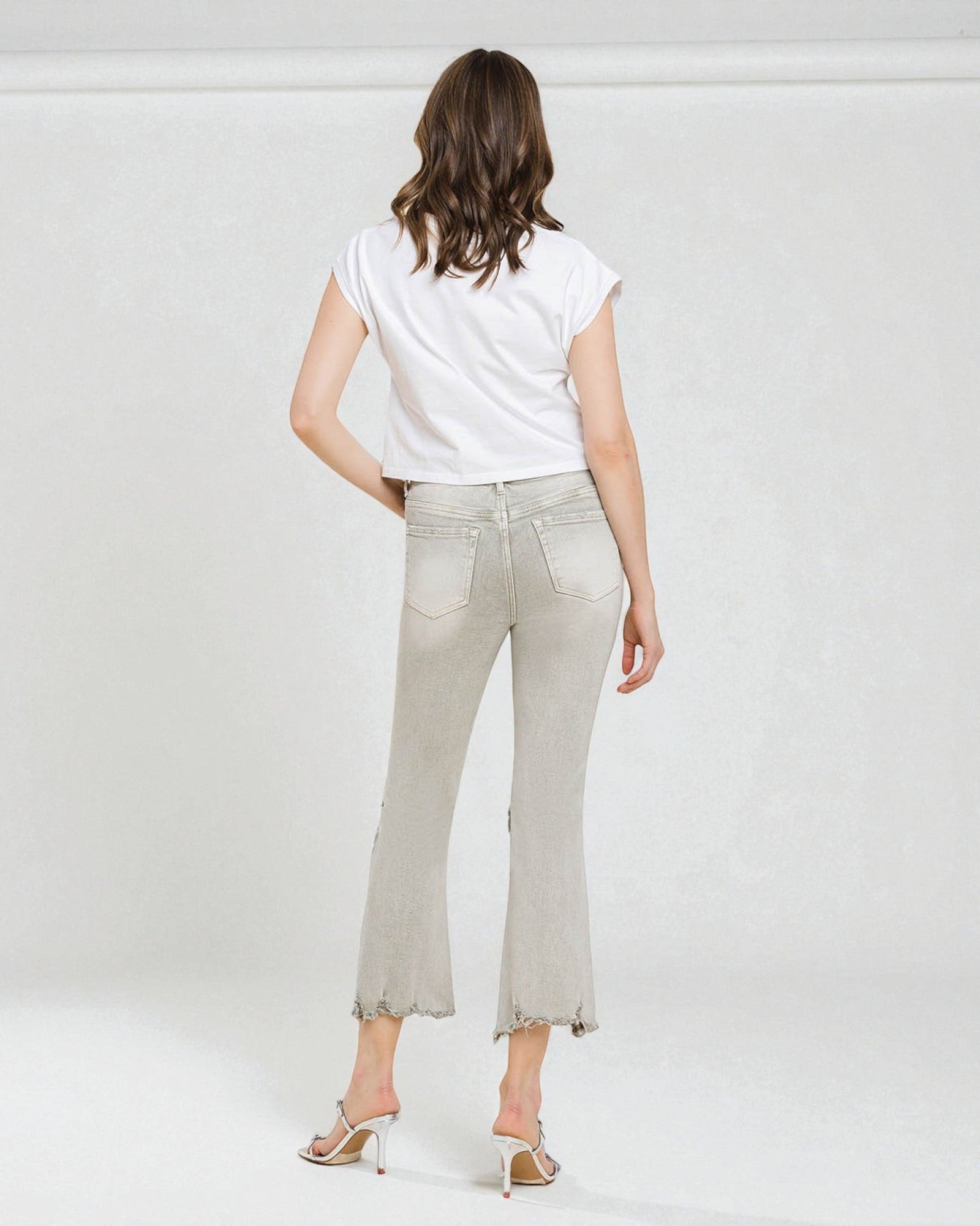 Woman wearing light-colored jeans and a white top on a plain background