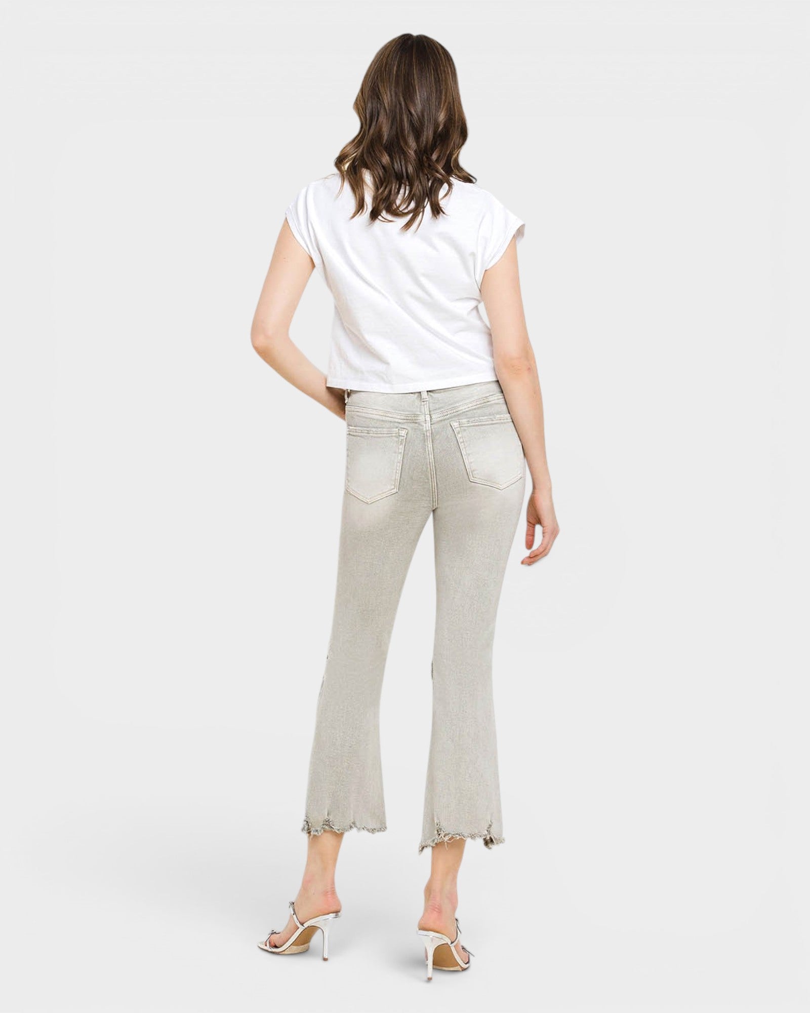 Woman wearing light gray jeans and a white top on a plain background
