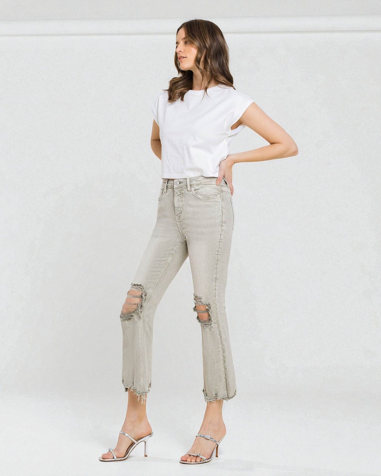 Woman wearing a white t-shirt and light gray ripped jeans against a white background