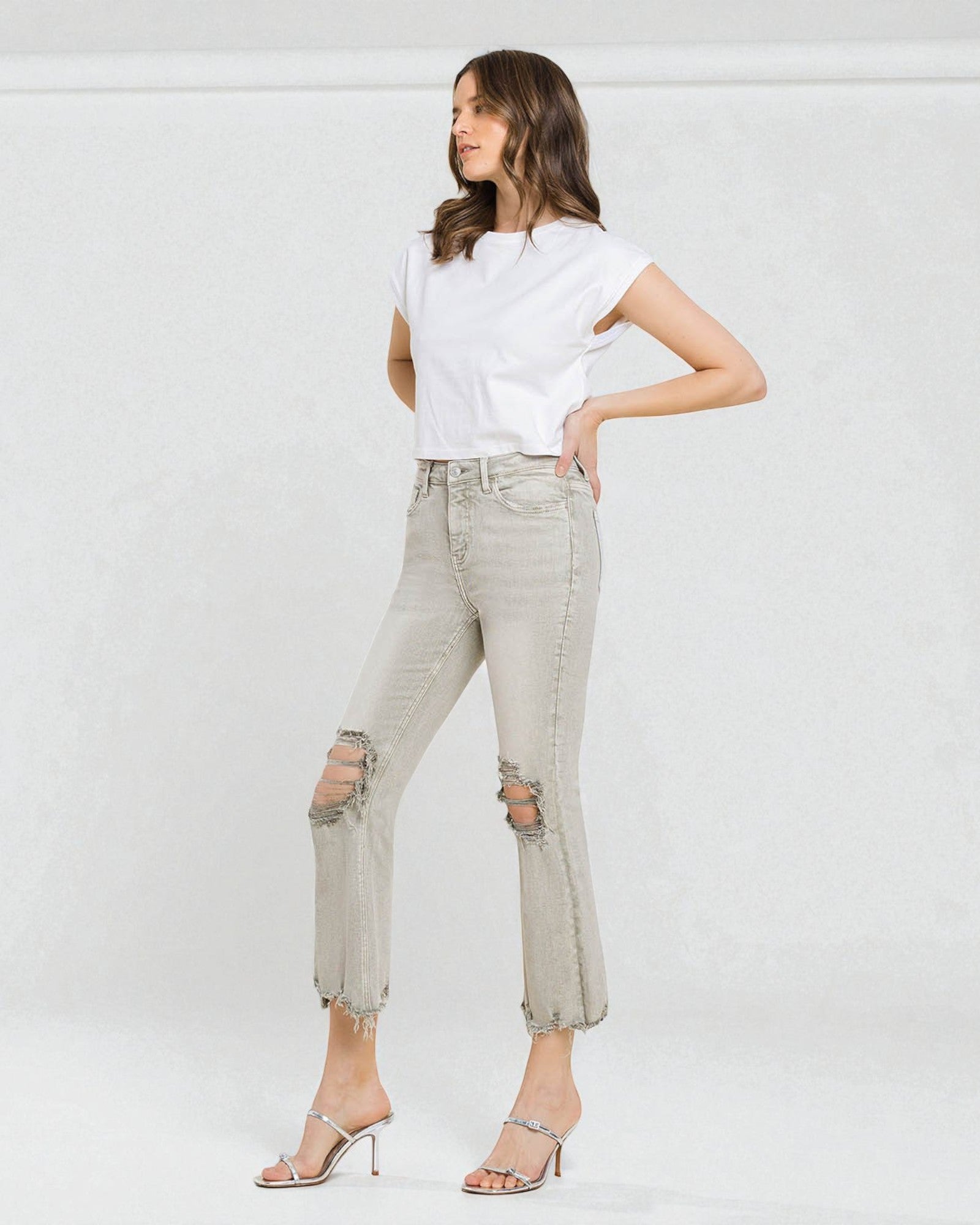 Woman wearing a white t-shirt and light gray ripped jeans against a white background