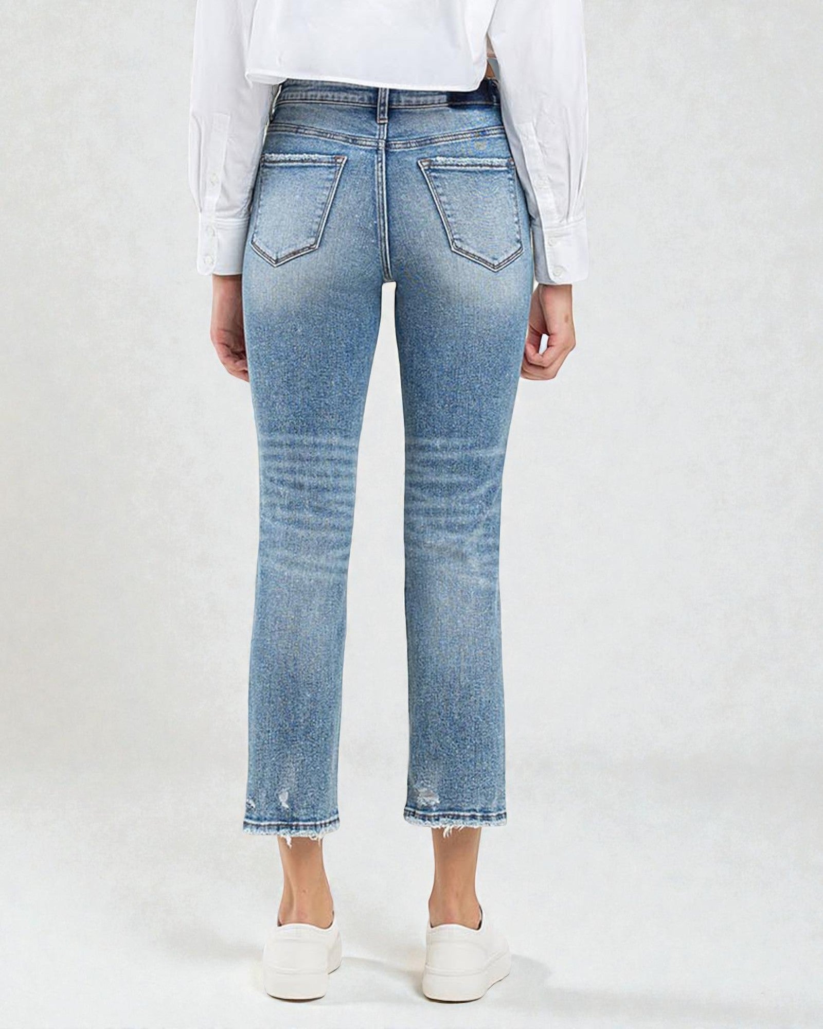 Person wearing light blue jeans and a white shirt on a plain background