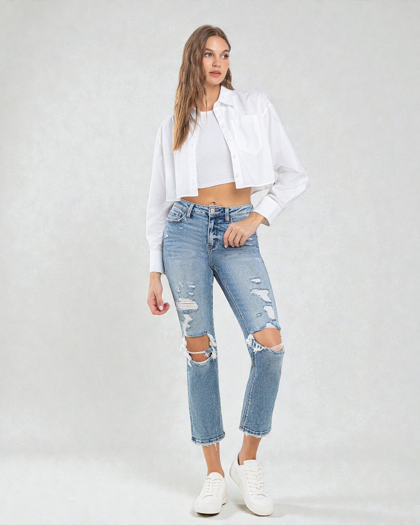 Woman wearing a white jacket and ripped jeans on a plain background
