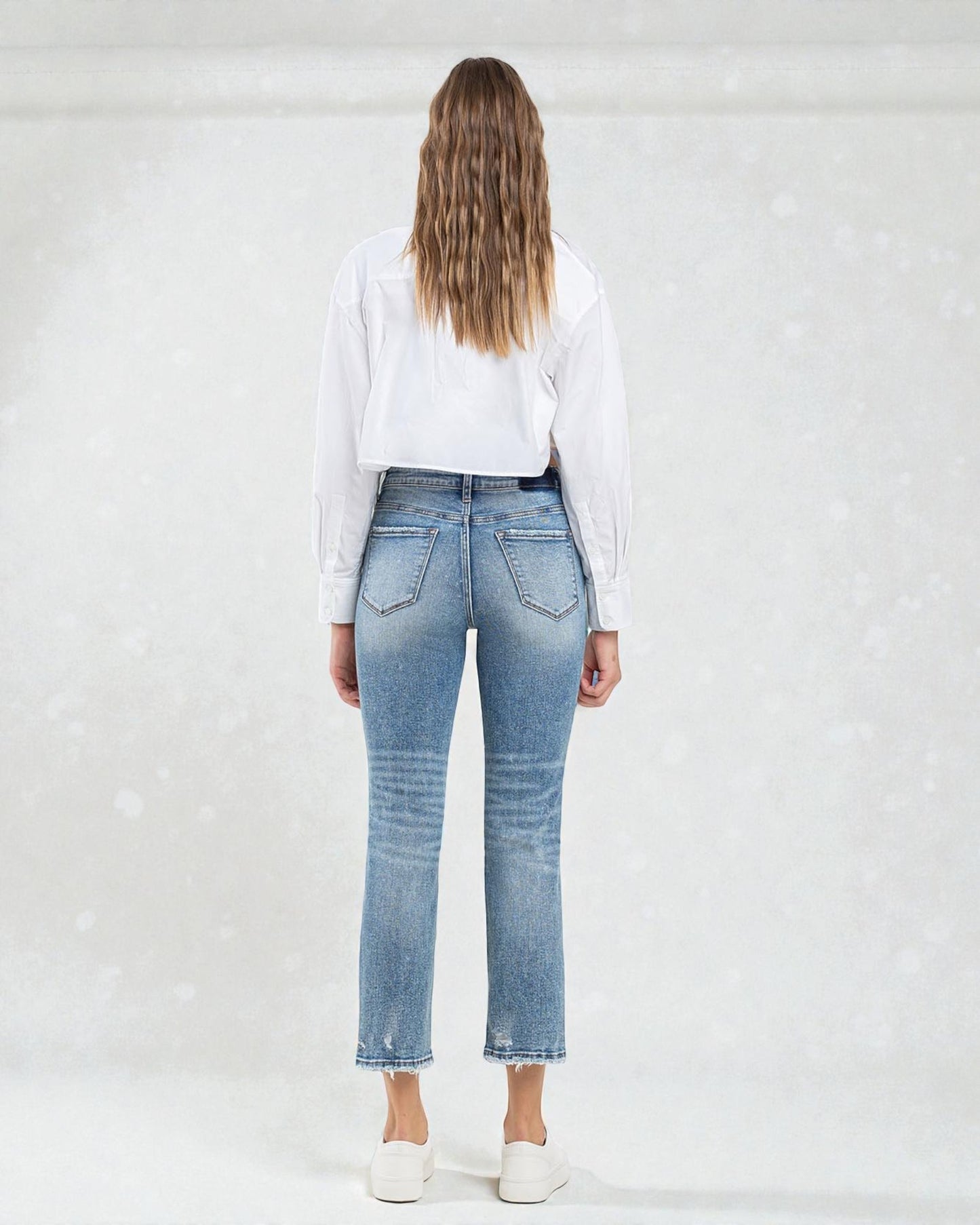 Person wearing blue jeans and a white shirt on a plain background